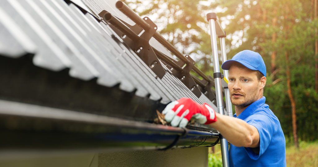 Man In A Blue Uniform Cleaning Gutters