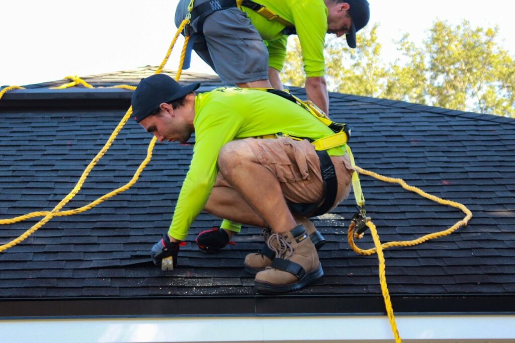 two professional roofers wearing safety harnesses attached to rope