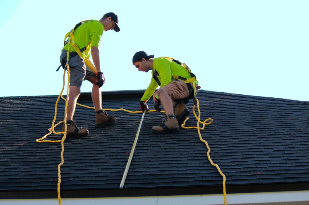 two roofers wearing safety harnesses measure a roof