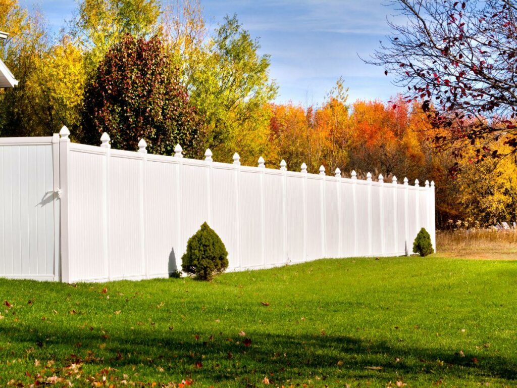 white vinyl fence on Long Island with a background of trees in fall colors