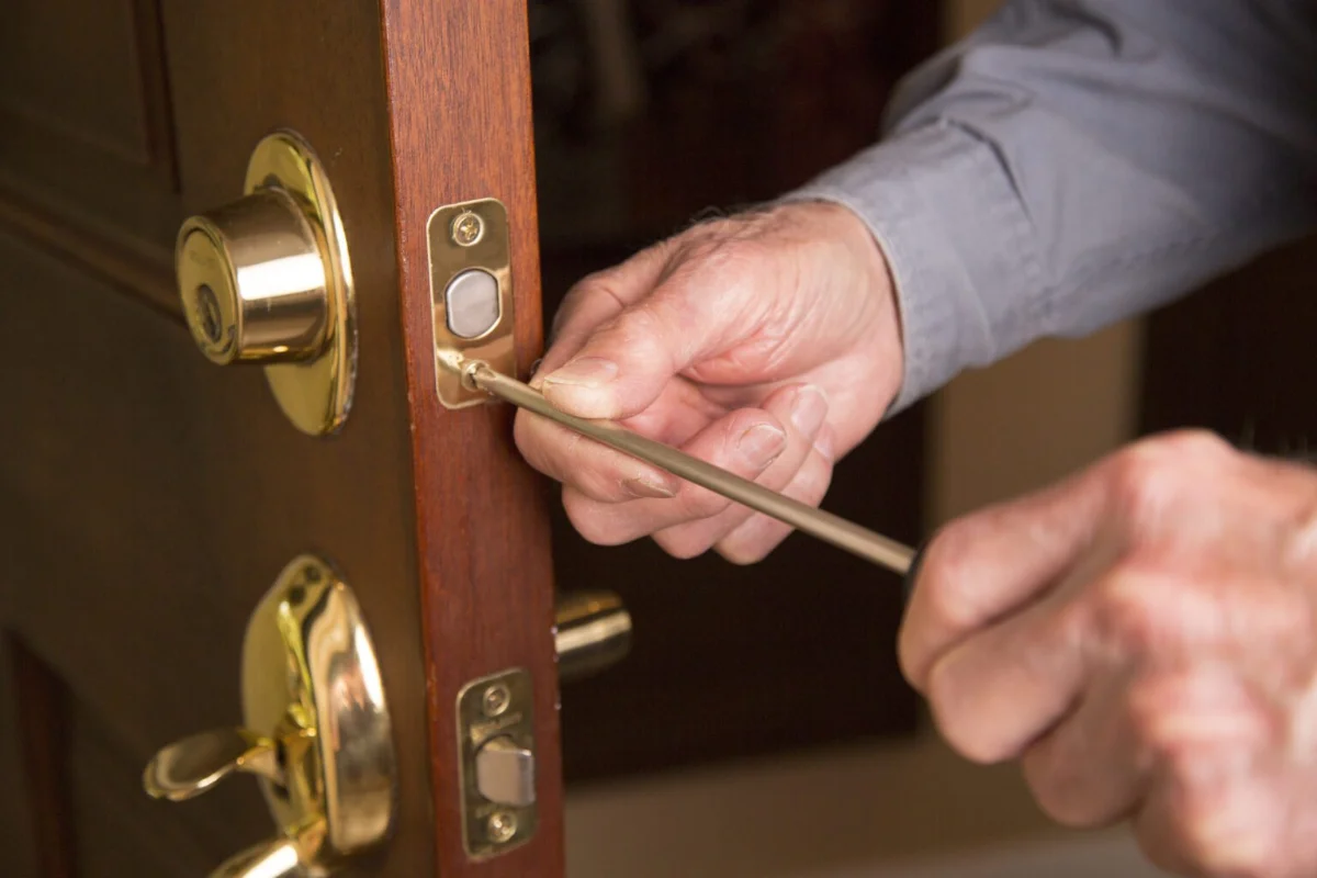 Locksmith or home owner installing or repairing new long on beautiful wood front door. He wears blue uniform shirt.