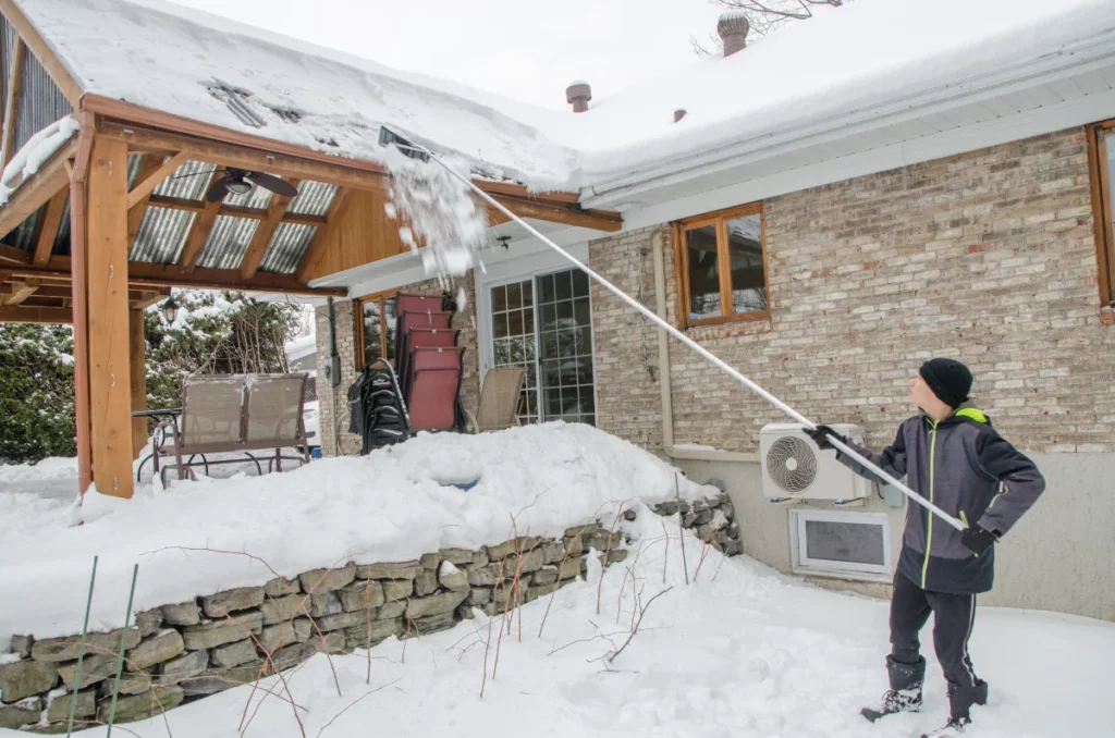 Teenage boy shoveling snow from patio rooftop during a day of winter
