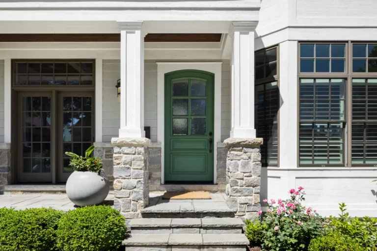 Front entry of a Long Island home with stone paver steps, green door, and stone pillars